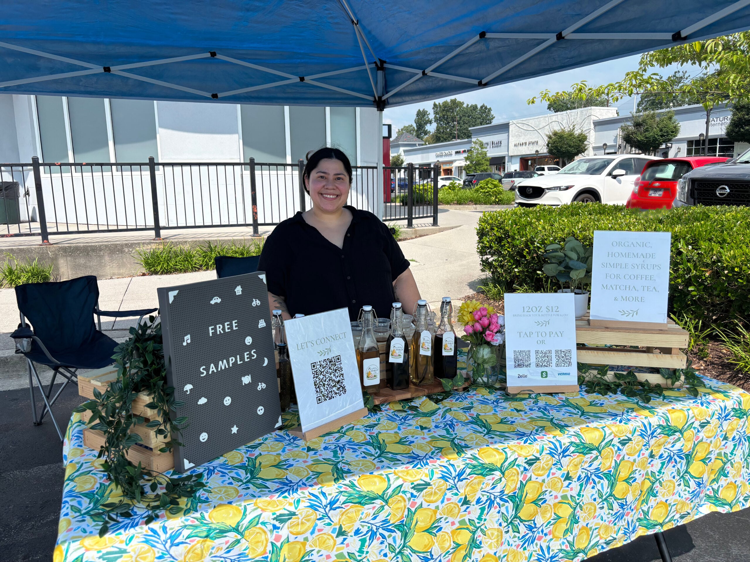 Simply Syrup by Yuri Pop Up booth with tent and table set up. Table decorated with plants, signage, and simple syrups for sale.