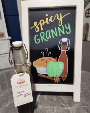 spicy granny apple simple syrup in glass bottle in front of sign with syrup name, apple pie, a green apple, and the syrup bottle drawn in chalk